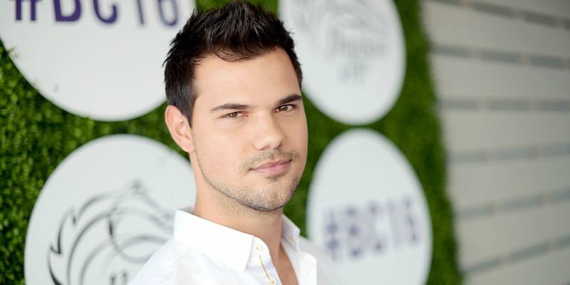 Taylor Lautner is smiling in a white shirt on the red carpet.