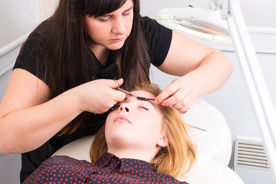Young Blond Woman Lying Down with Eyes Closed and Having Eyebrows Trimmed