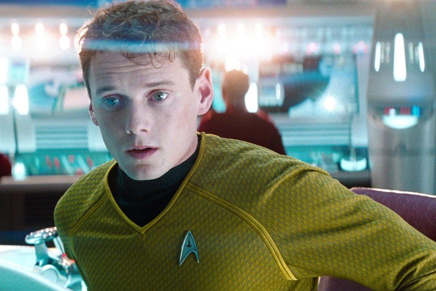 Anton Yelchin sits in a chair and looks off camera in Star Trek