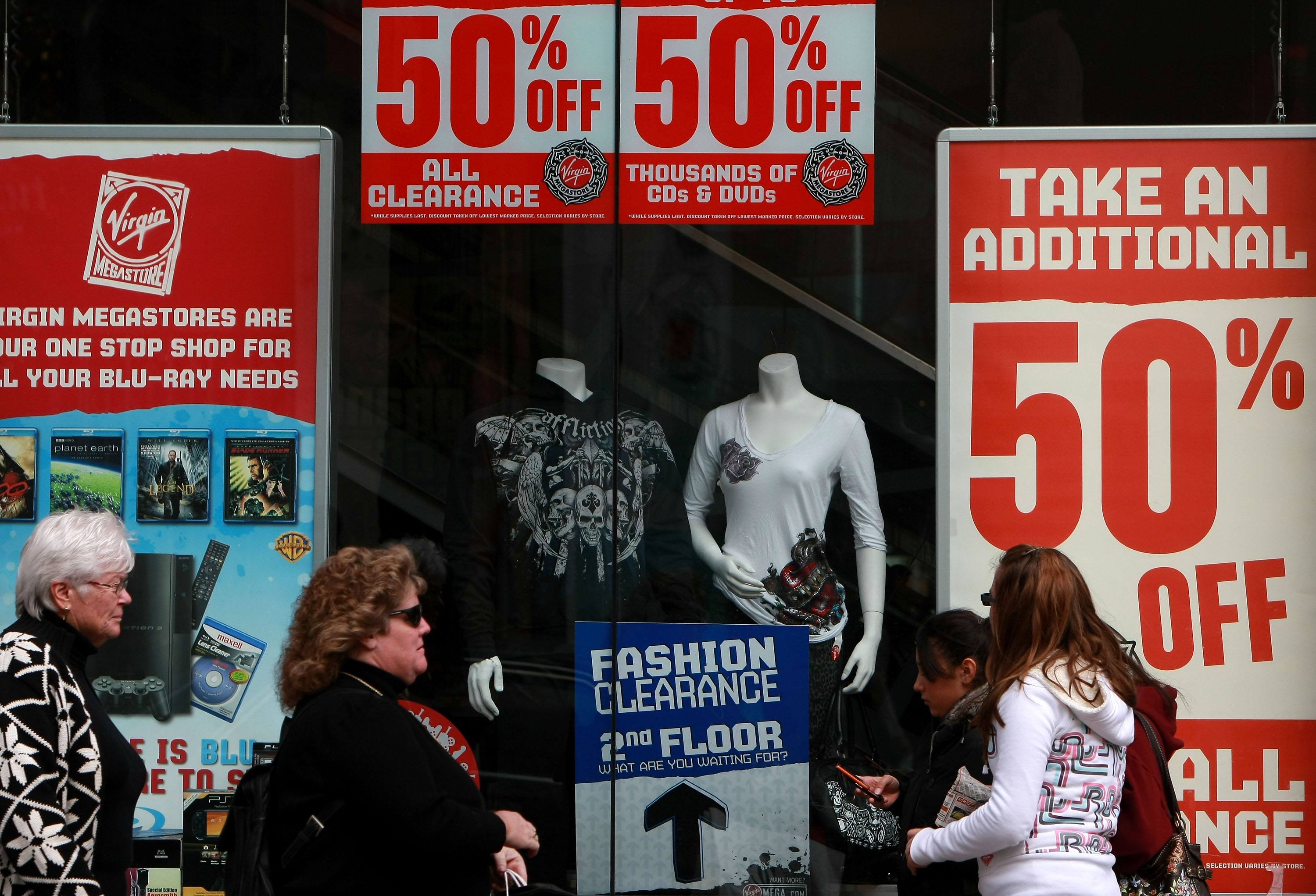 Pedestrians walk by sale signs looking for deals and the best ways of saving money in the retail sector