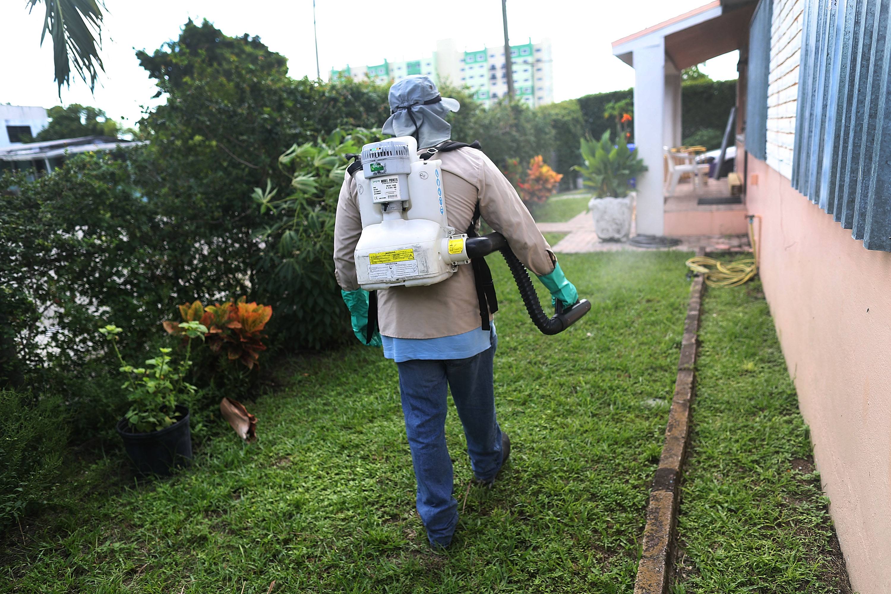 A man sprays pesticide around a building