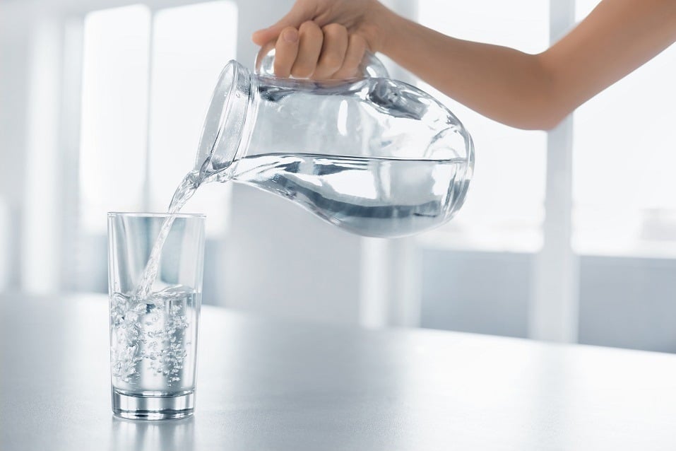woman's hand pours water from a pitcher into a glass