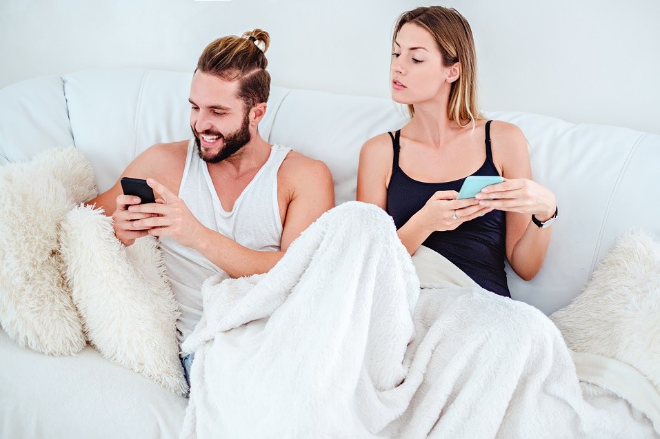 A woman looks over her boyfriend's shoulder to see what he is typing on his smartphone