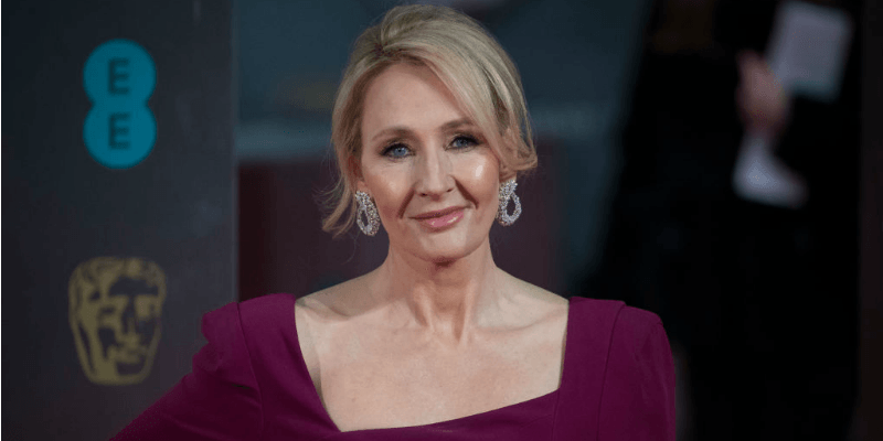 J.K. Rowling in a purple dress smiling at the camera.