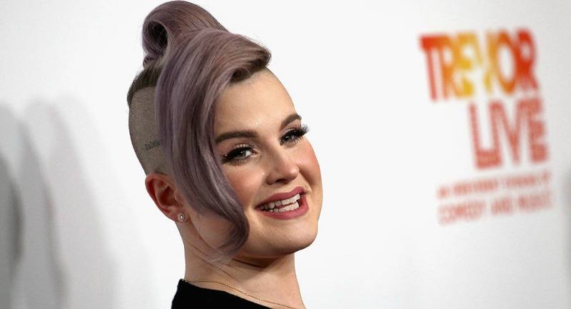 Kelly Osbourne smiles and looks over to the side as she poses for photos at a red carpet event. 