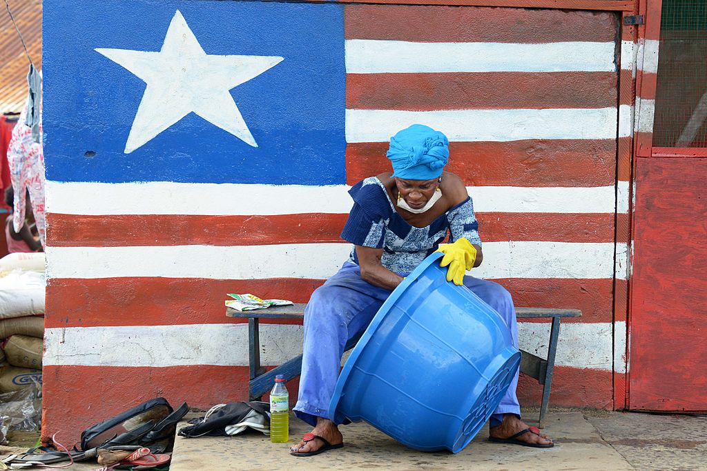 A woman sitting by a mural showing Liberia's national flag