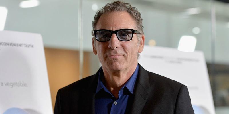 Michael Richards is in a black suit and is wearing black rimmed glasses.