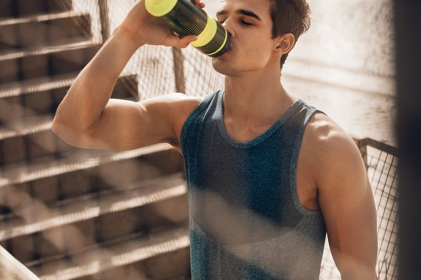 A muscular young man drinks water from a yellow water bottle
