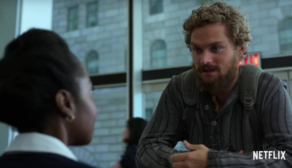Finn Jones as Danny Rand in Iron Fist standing in front of a woman smiling with a building in the background