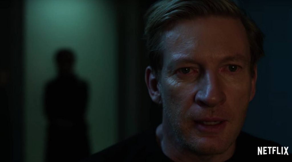 David Wenham looking scared while a mysterious figure lingers in the background on Iron Fist