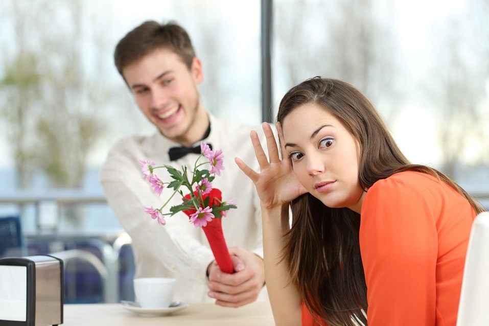 A woman makes an exasperated face on the side as a young man offers her flowers