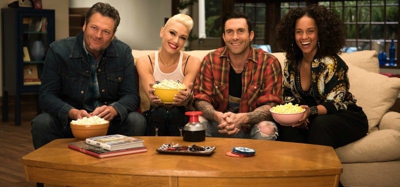 Blake Shelton, Gwen Stefani, Adam Levine, and Alicia Keys sitting on a coach holding bowls of popcorn.