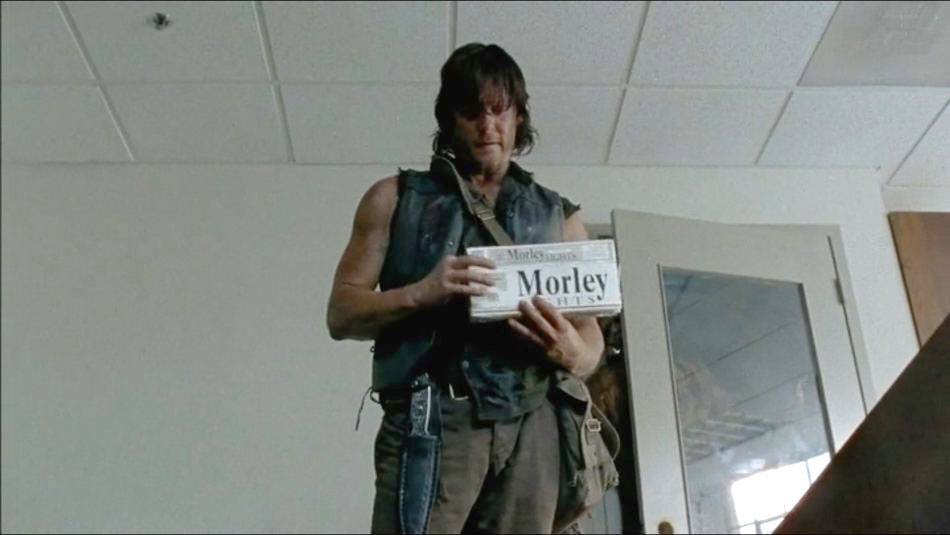 Daryl is standing in a room holding up something that says "Morley." Daryl is standing in a room holding up something that says "Morley."