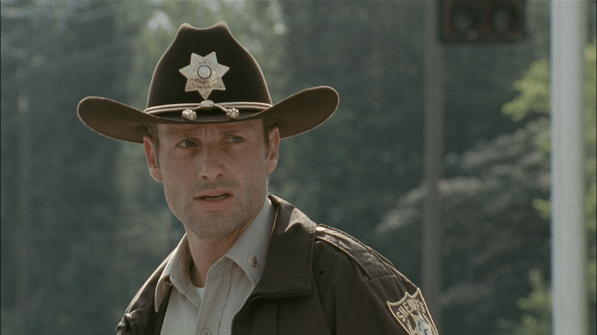 Rick Grimes, wearing a sheriff's outfit, and looking to his left. Rick Grimes, wearing a sheriff's outfit, and looking to his left.
