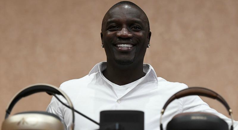 Akon is smiling as he is sitting down.