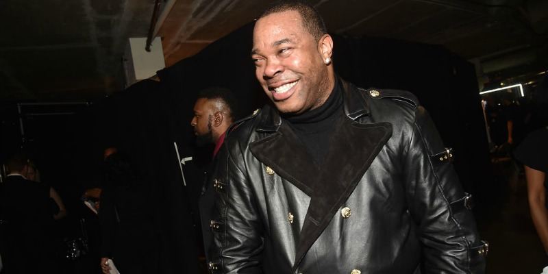 Busta Rhymes is smiling wearing an all black outfit.