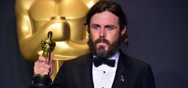 Casey Affleck is holding up his Oscar in a tux.