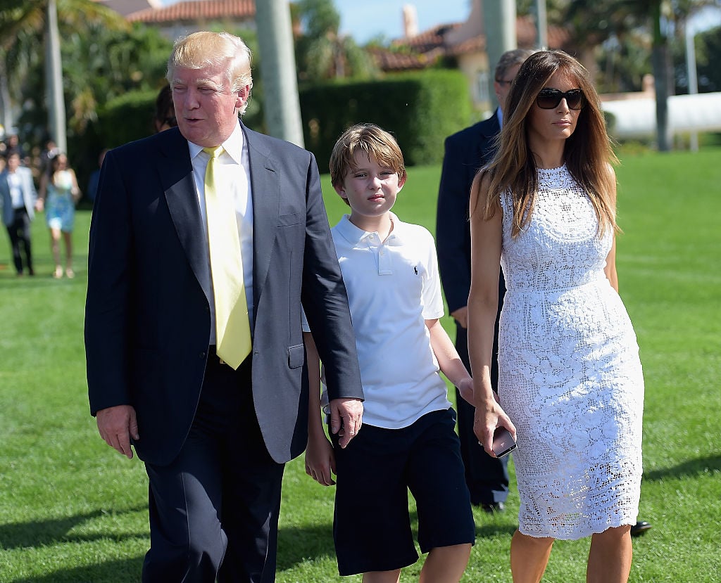 Donald Trump, Barron Trump and Melania Trump walking together across a green lawn. 