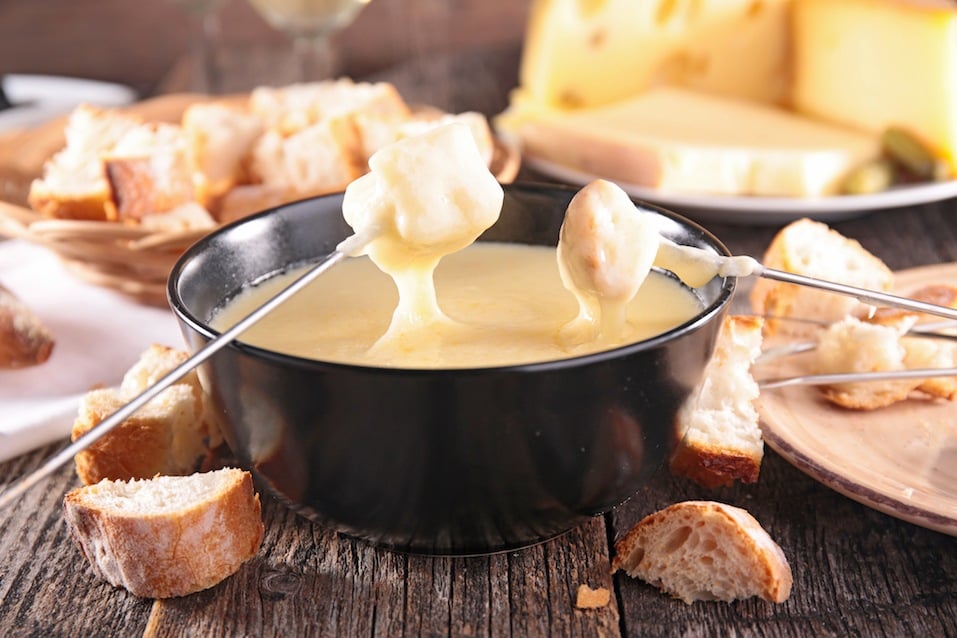 Dipping bread into a bowl filled with cheese fondue.