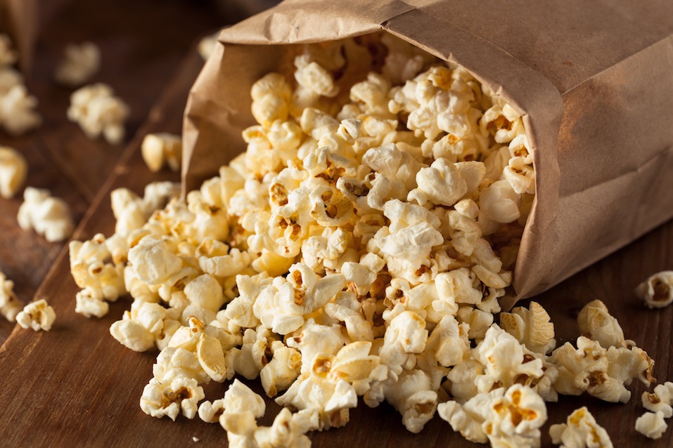 Freshly made popcorn spilling out of a paper bag onto a table.