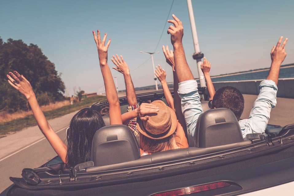 Young happy people enjoying road trip in their convertible and raising their arms up