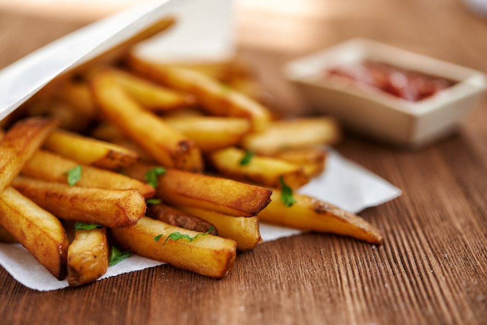Container of french fries lying sideways on a table with container of ketchup next to it. Container of french fries lying sideways on a table with container of ketchup next to it.