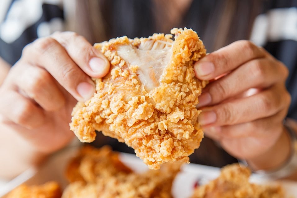 Two hands holding a piece of crispy fried chicken