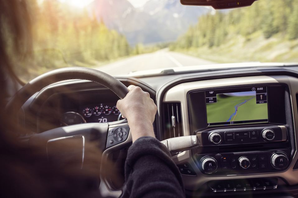 Woman holding the steering wheel driving a car on a rural road through the mountains