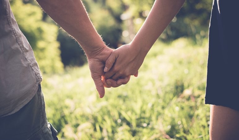Couple holding hands while walking through tall grass. Couple holding hands