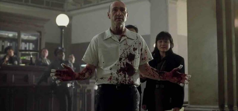 John Doe has his arms up as if to surrender as he is covered in blood.