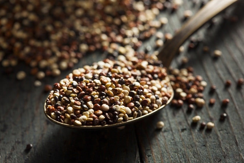 Raw quinoa sitting in a serving spoon and scattered around a table top.
