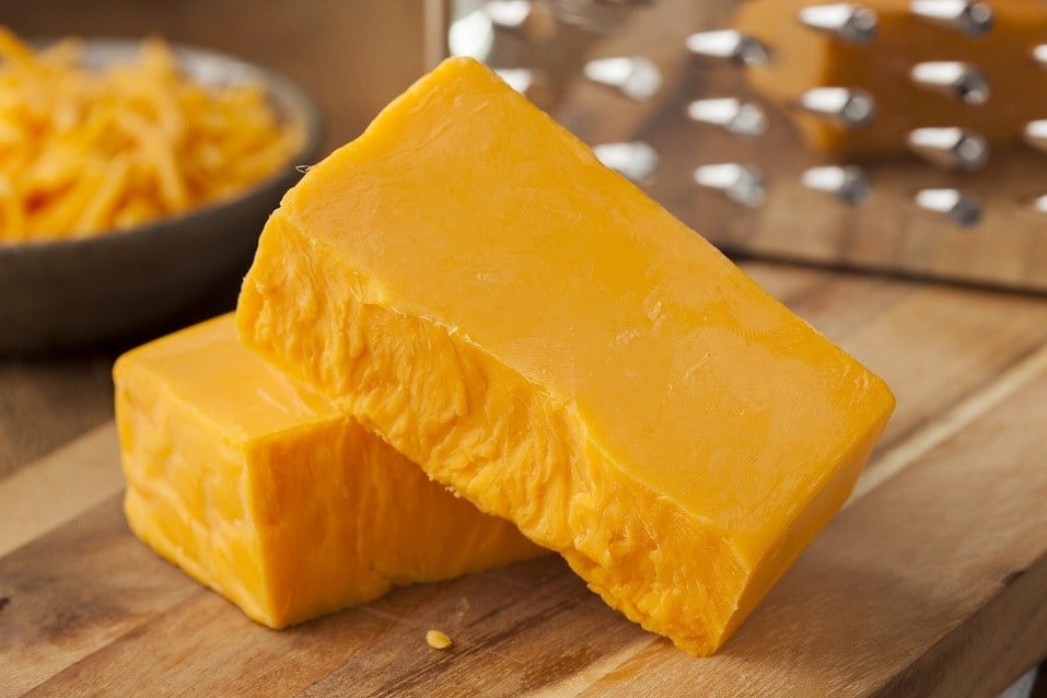 Organic sharp Cheddar cheese on a wooden cutting board.