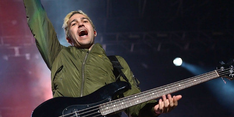 Pete Wentz is playing bass on stage and has one hand in the air.