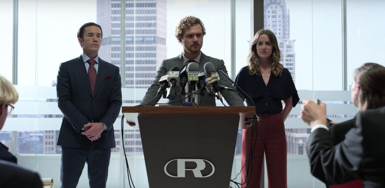 Tom Pelphrey, Finn Jones and Jessica Stroup standing behind a podium in the middle of a press conference in Iron Fist