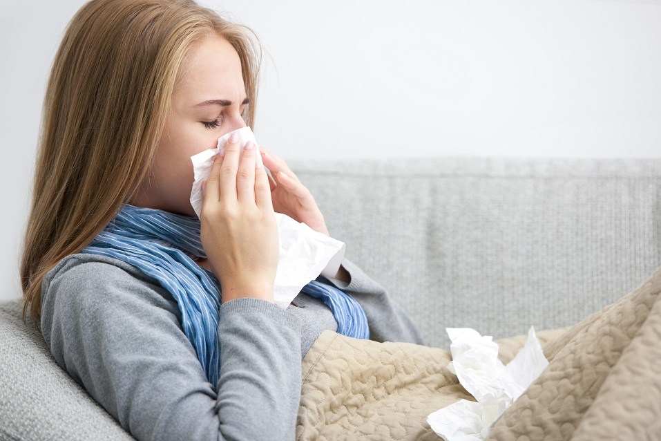 Woman sneezing into a tissue while sitting on a couch. Woman sneezing into a tissue while sitting on a couch.