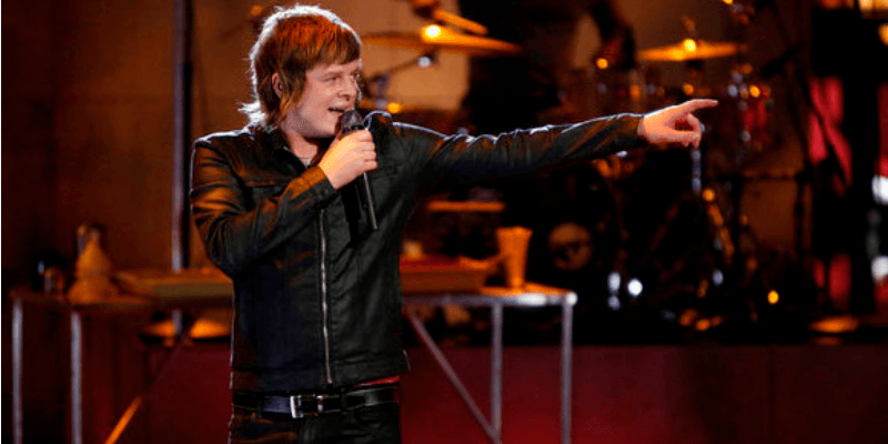 Terry McDermott is singing on stage and pointing to the left.