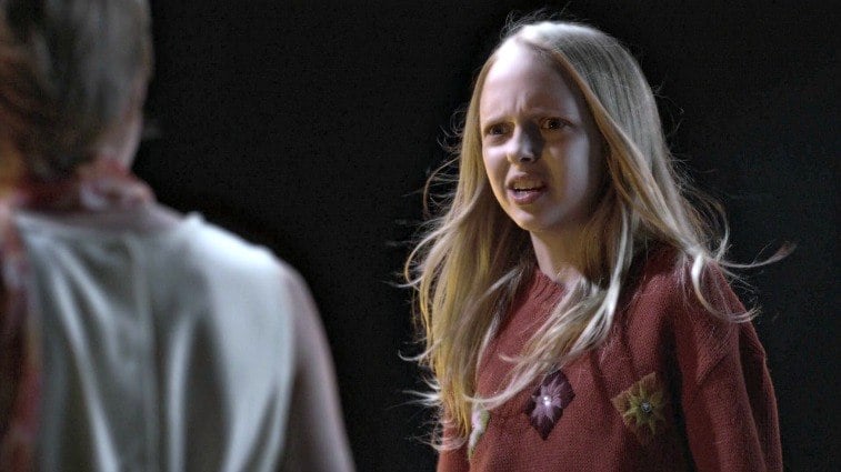 Young blonde girl Bethany Young in red sweater talking to another child in the darkness