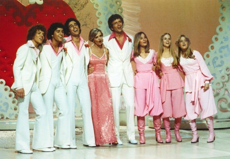 Eight-person family on stage in white and pink attire with Valentine's decorations behind them