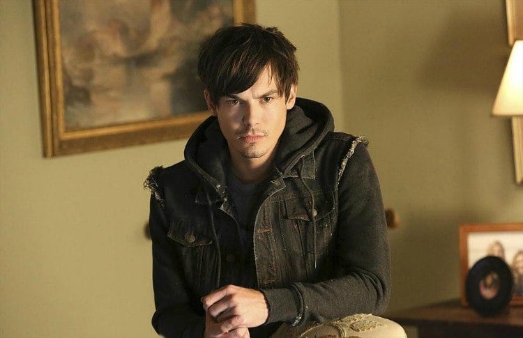 Caleb Rivers young man in a black hoodie and black denim vest in a tan room with a framed painting