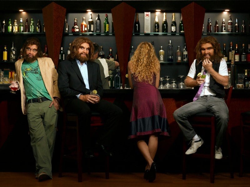 Three well-dressed cavemen in a bar with a woman facing away