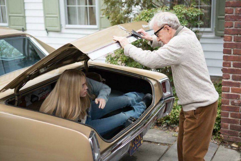 A man standing over a car looking in the trunk at a girl