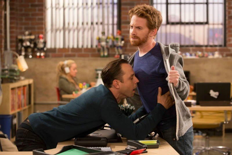 Two men in an office one is leaning over a desk with his hands on the other's chest