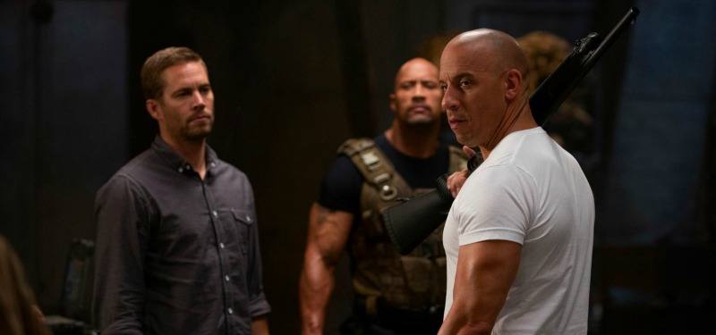 Brian, Dom, and Hobbs are standing together looking serious.