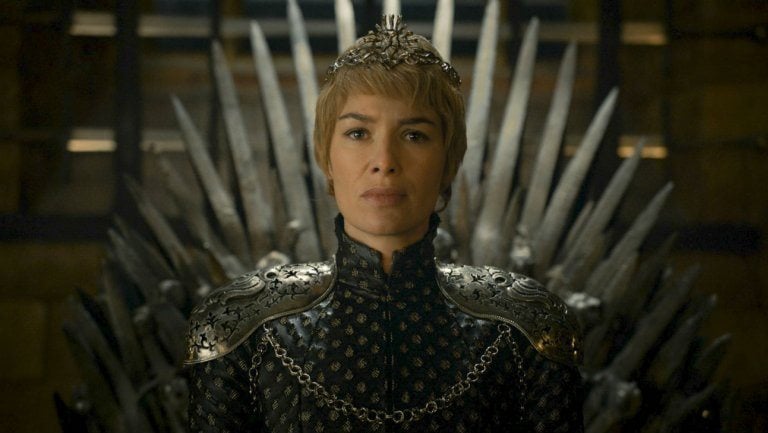 Lena Headey as Cersei Lannister in all black, wearing a crown, and sitting atop the Iron Throne in Game of Thrones.