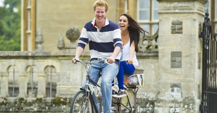 A man and a woman on a tandem bicycle riding outside a castle