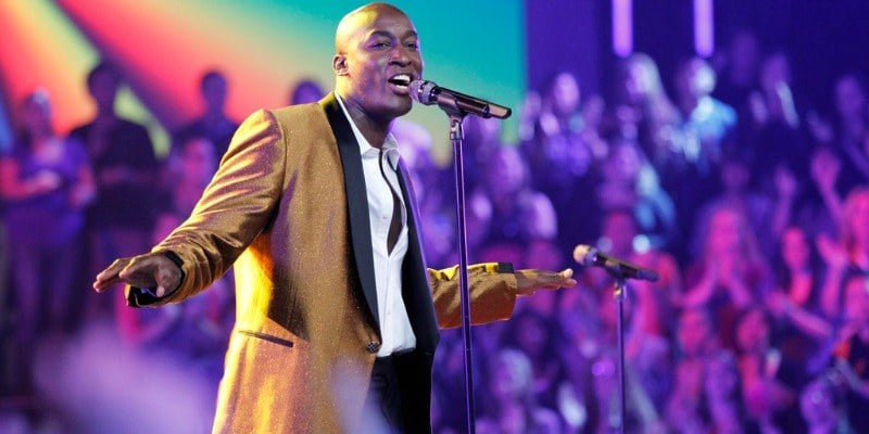 Jermain Paul is singing in a suit on stage of the show.