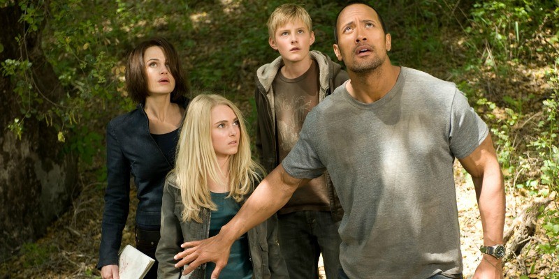 Dwayne Johnson is looking up at the sky as he has his arm out stopping the rest of the group.