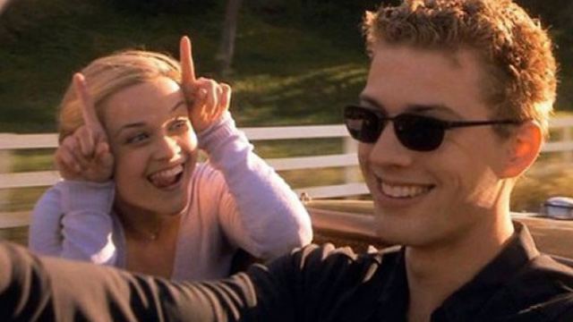 Reese Witherspoon laughing with her fingers pointed up, while Ryan Phillippe drives