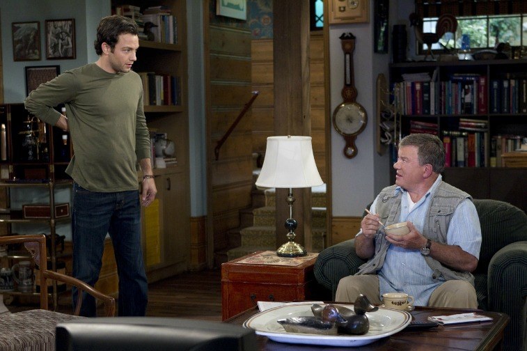 A young man standing and looking at his father, who is sitting in a char