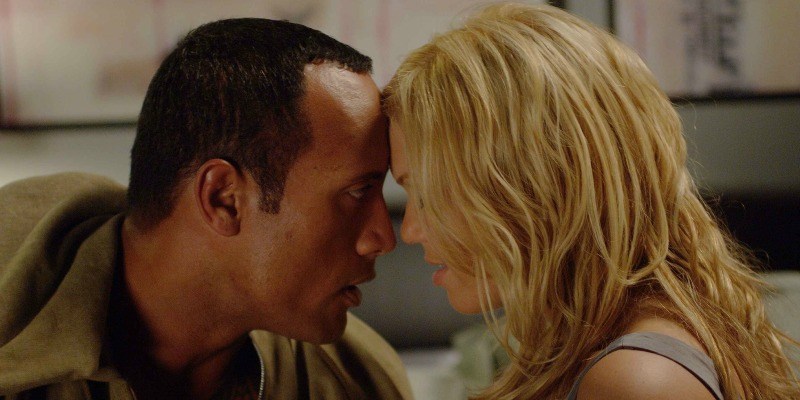 Dwayne Johnson and Mandy Moore are looking at each other with their heads touching.